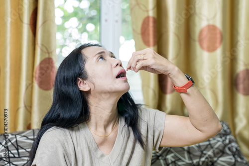 A Asian woman is holding a medical pill capsule as a dietary supplement and is considering taking or consuming vitamin C and D to treat and strengthen her skin, hair, and nails.