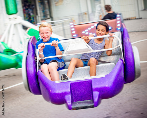 Two diverse kids riding an amusement park ride at the fun theme park. Screaming, laughing and having a great time on a thrilling carnival ride. Intentional motion blur on the image photo