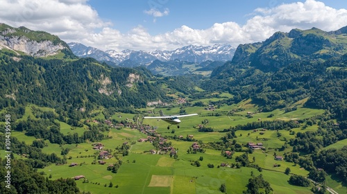 Aerial view of lush green valleys surrounded by majestic mountains under a bright blue sky.