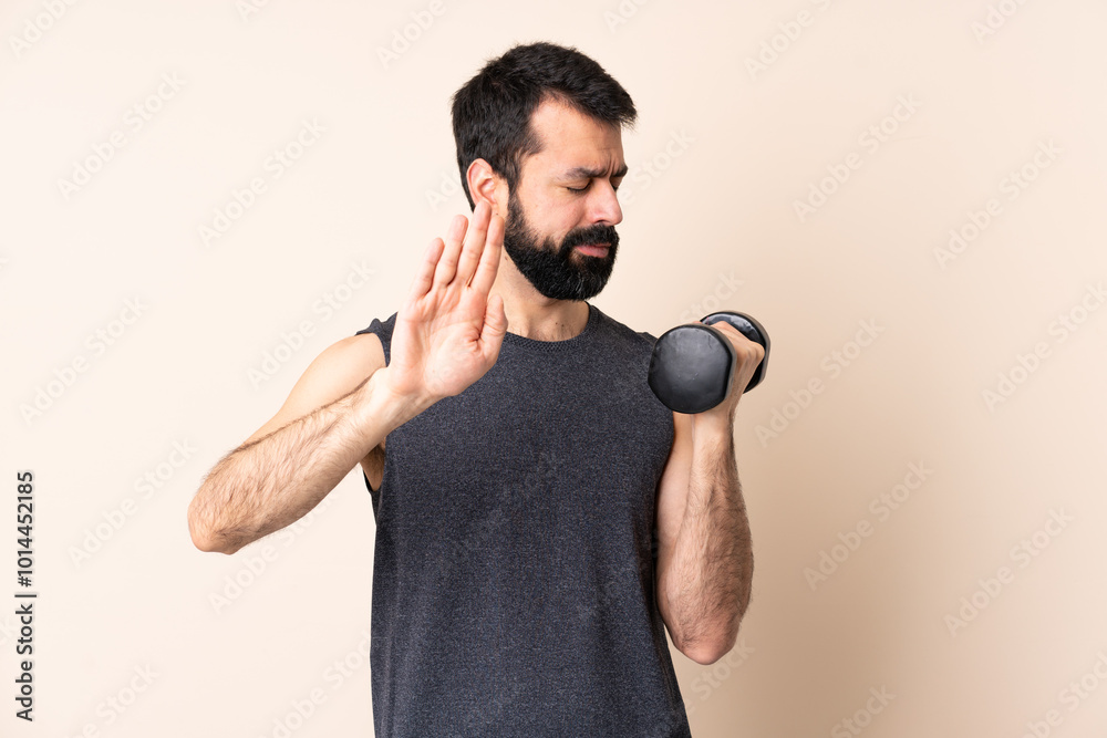 Caucasian sport man with beard making weightlifting over isolated background making stop gesture and disappointed