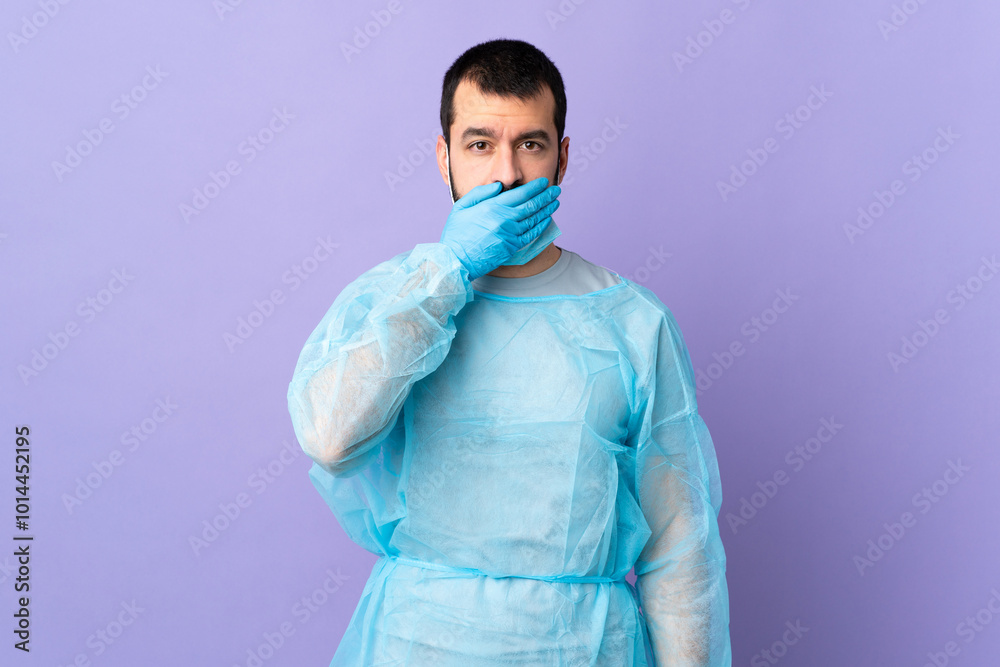Surgeon man with beard with blue uniform over isolated purple background covering mouth with hand Surgeon man with beard with blue uniform over isolated purple background covering mouth with hand