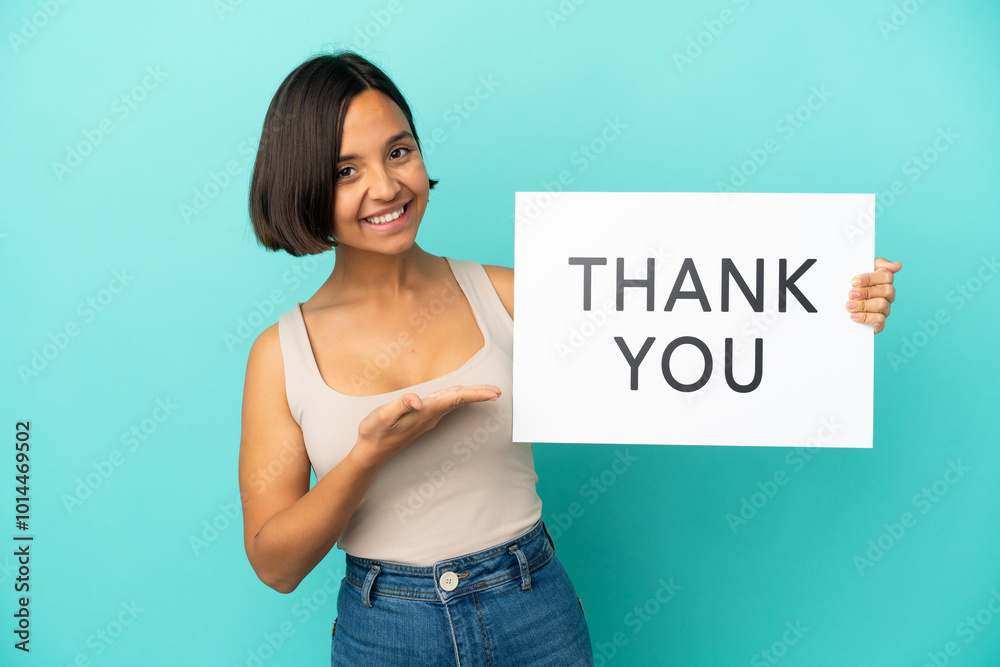 Young mixed race woman isolated on blue background holding a placard with text THANK YOU and pointing it Young mixed race woman isolated on blue background holding a placard with text THANK YOU and pointing it