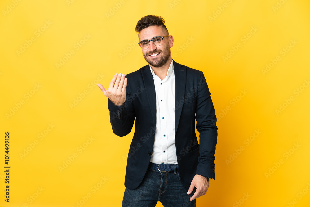 Businessman over isolated yellow background inviting to come with hand. Happy that you came Businessman over isolated yellow background inviting to come with hand. Happy that you came