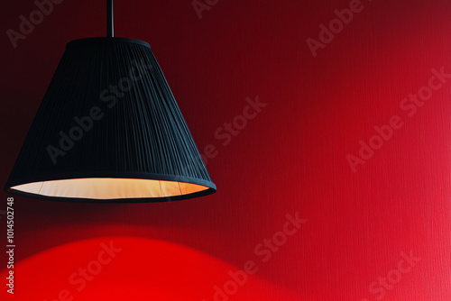 A black pendant lamp casts a warm glow against a vibrant red wall, creating a striking visual contrast.