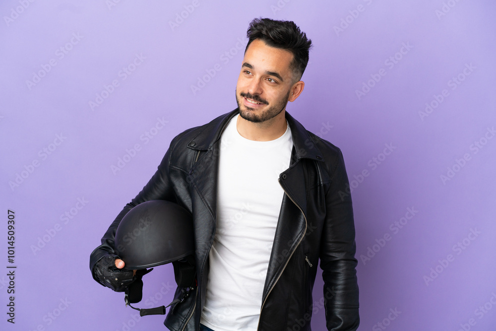 Fototapeta premium Young man with a motorcycle helmet isolated on purple background looking to the side and smiling
