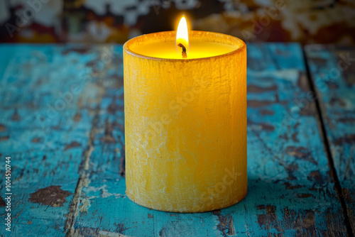 A lit yellow candle on a textured blue wooden surface, creating a warm and inviting atmosphere. photo