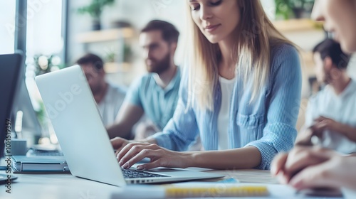 Woman Typing on Laptop with Blurry Background of Colleagues in Office