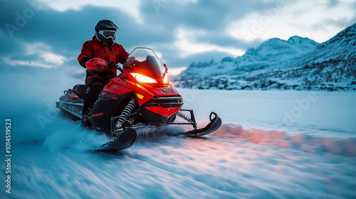 Man wearing winter gear is riding a snowmobile at high speed on snow with mountains in the background photo
