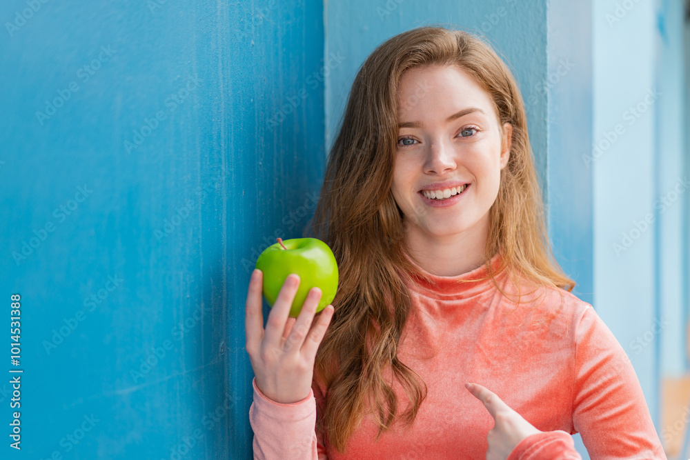 Young redhead woman with an apple at outdoors with surprise facial expression Young redhead woman with an apple at outdoors with surprise facial expression