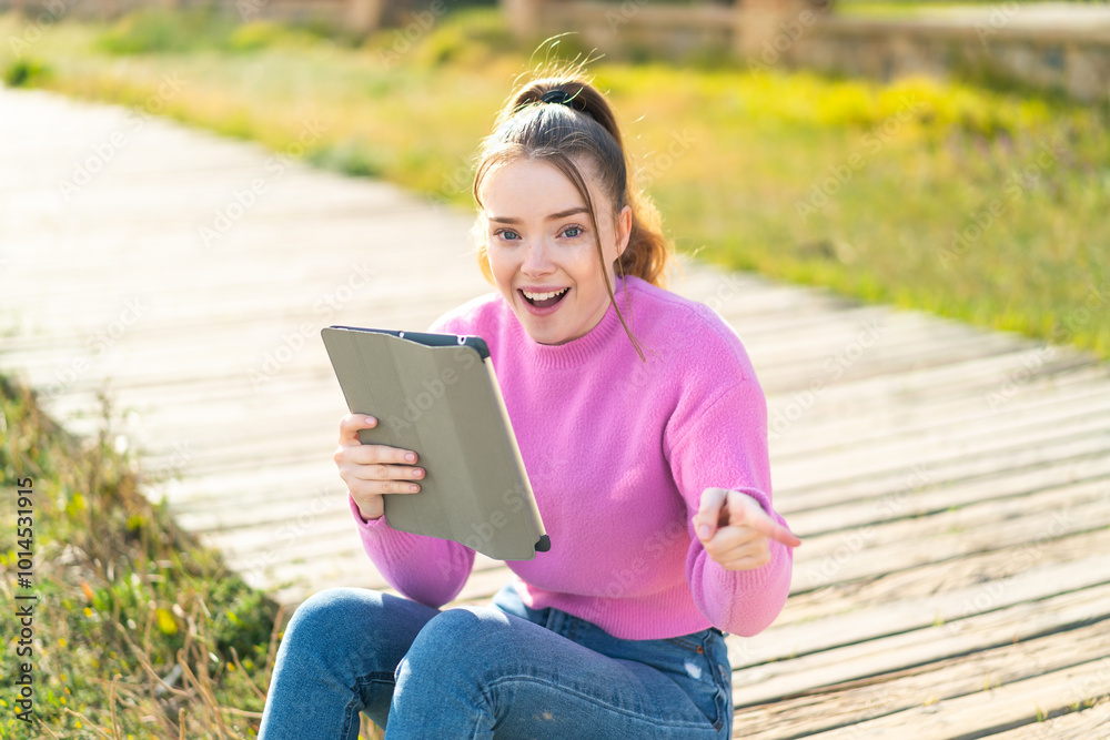 Fototapeta premium Young pretty girl holding a tablet at outdoors surprised and pointing finger to the side