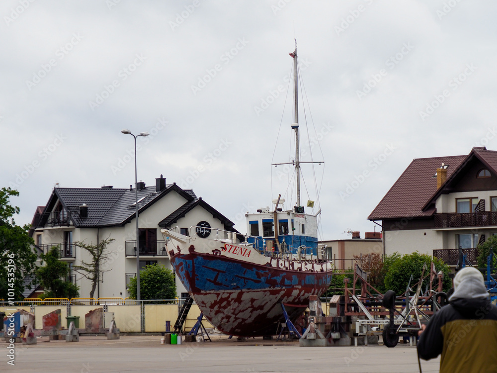 Old Fishing Boat on Land in Front of Buildings Old Fishing Boat on Land in Front of Buildings