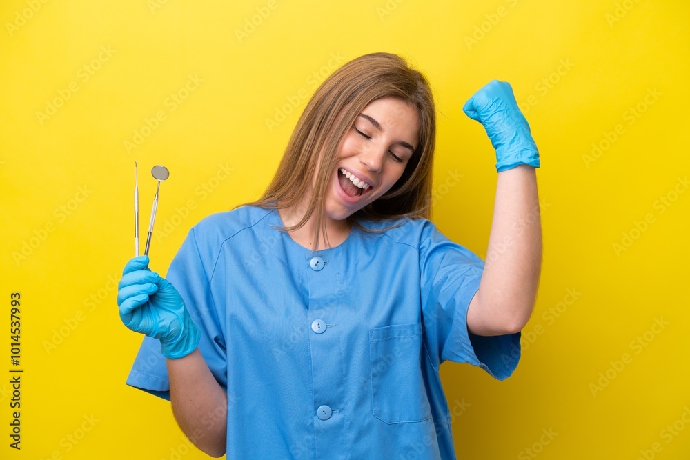 Dentist caucasian woman holding tools isolated on yellow background celebrating a victory Dentist caucasian woman holding tools isolated on yellow background celebrating a victory