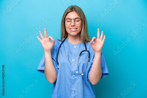 Young surgeon doctor woman isolated on blue background in zen pose