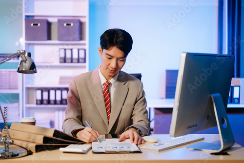 Asian Businessman analyzing reports in a modern office, working on a computer. Perfect for corporate, business, and over time concepts