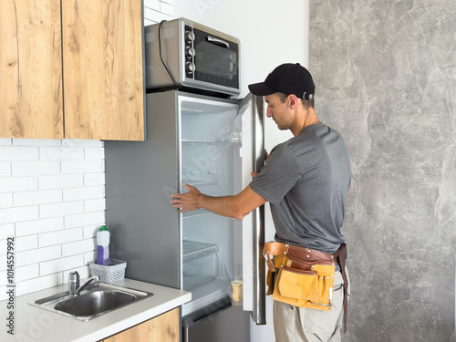 Male technician with screwdriver repairing refrigerator indoors