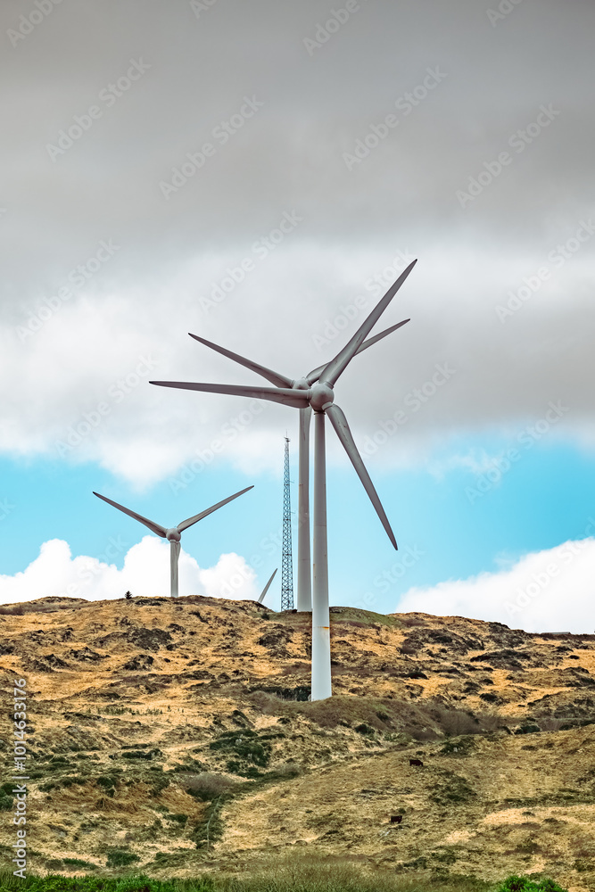 A group of wind turbines are placed on a hilltop, with a cloudy sky above. A group of wind turbines are placed on a hilltop, with a cloudy sky above.