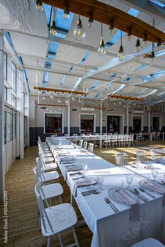 Obraz na płótnie A bright, glass-walled banquet hall with tables covered with white tablecloths. Tableware ready to serve dishes. Photo taken during the day, with sunlight streaming in. w salonie