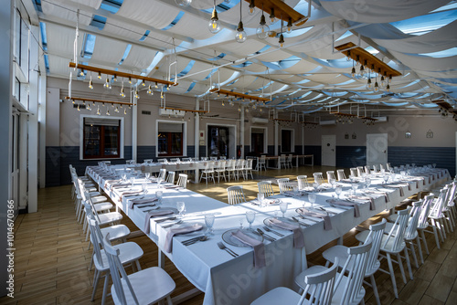 Obraz na płótnie A bright, glass-walled banquet hall with tables covered with white tablecloths. Tableware ready to serve dishes. Photo taken during the day, with sunlight streaming in. w salonie