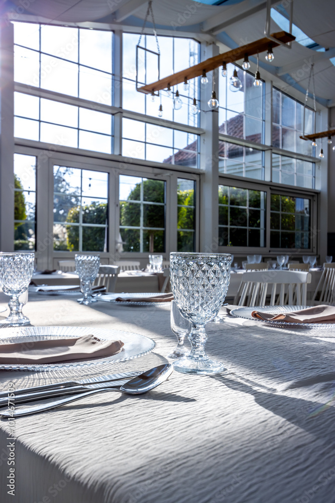 Crystal glass on the table in a bright, glass-walled banquet hall. Photo taken during the day, with sunlight streaming in.