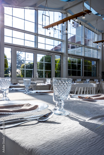 Crystal glass on the table in a bright, glass-walled banquet hall. Photo taken during the day, with sunlight streaming in.
