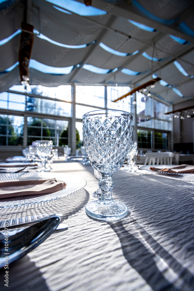 Crystal glass on the table in a bright, glass-walled banquet hall. Photo taken during the day, with sunlight streaming in.