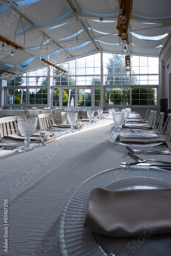 Obraz na płótnie A bright, glass-walled banquet hall with tables covered with white tablecloths. Tableware ready to serve dishes. Photo taken during the day, with sunlight streaming in. w salonie