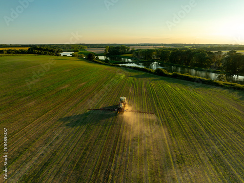 Drone shot of a tractor spraying in lush green wheat fields under the bright sun, showcasing modern agriculture
