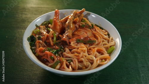 a typical Indonesian food called mie ayam ceker in a bowl on a green wooden board. Indonesian culinary, street culinary, street food, spicy noodles, noodles with chicken feet, chicken noodle photo