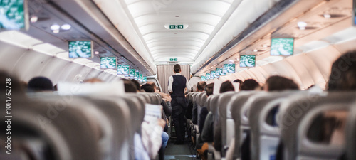 Interior of airplane with passengers on seats and stewardess in uniform walking the aisle, serving people. Commercial economy flight service concept photo