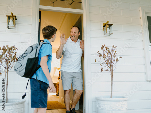 Young boy waving his hand goodbye to his dad at the doorway. photo