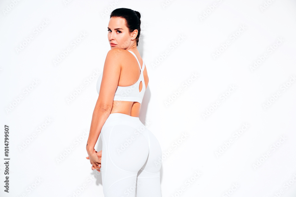 Fitness confident woman in white sports clothing. Sexy young beautiful model with perfect body. Female isolated on white wall in studio. Stretching out before training. Turns around Fitness confident woman in white sports clothing. Sexy young beautiful model with perfect body. Female isolated on white wall in studio. Stretching out before training. Turns around