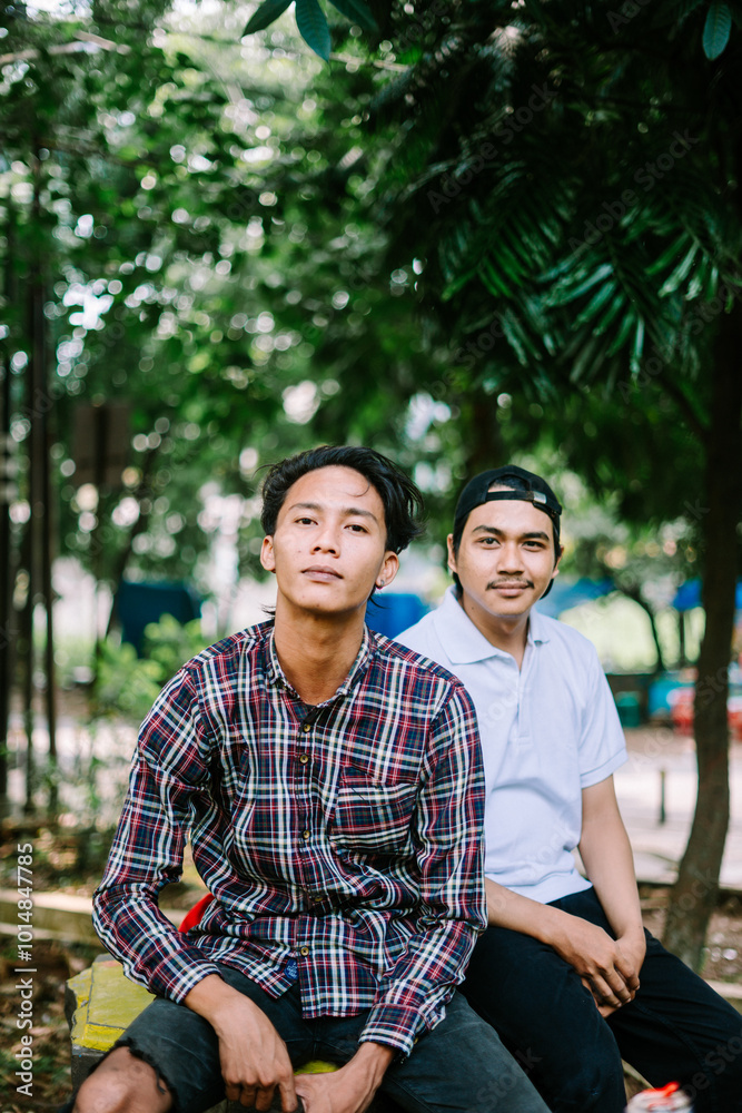 Two Southeast Asian men sitting in a city square, capturing a moment of relaxation and conversation Two Southeast Asian men sitting in a city square, capturing a moment of relaxation and conversation