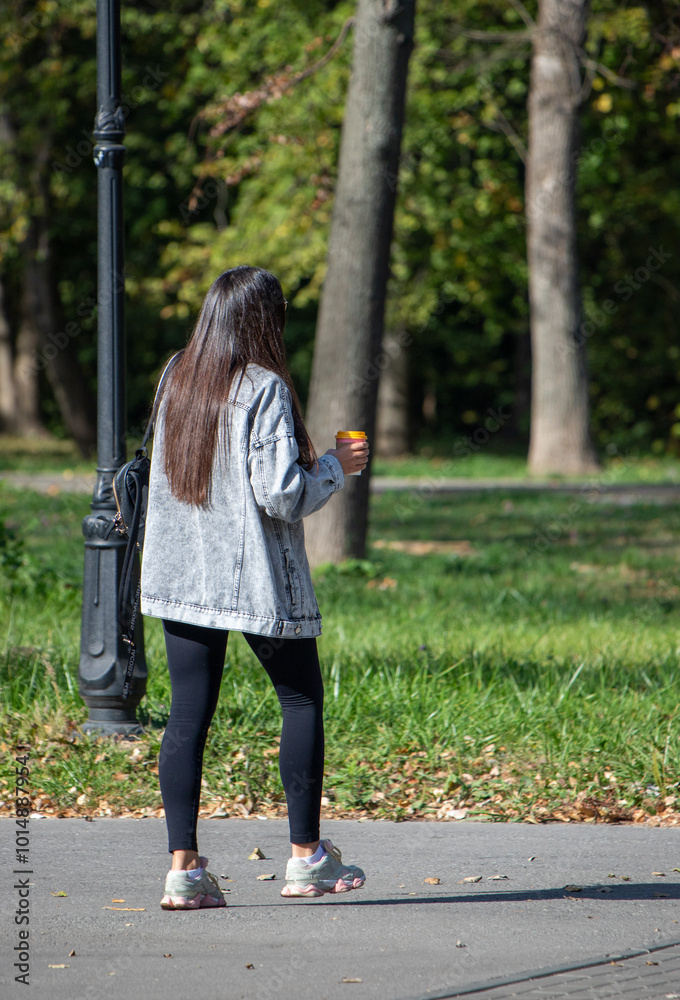 A woman is walking down a path with a cup of coffee in her hand A woman is walking down a path with a cup of coffee in her hand
