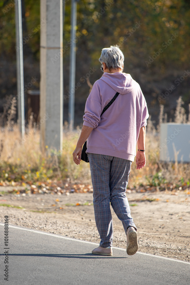 A woman in a purple hoodie and gray pants walks down a road A woman in a purple hoodie and gray pants walks down a road
