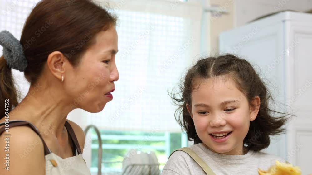 Lively moment of mother and daughter in kitchen, young girl playfully eating bread while laughing and feeding snack to mom. joyful bonding relationship, family lifestyle at home laughter, and fun Lively moment of mother and daughter in kitchen, young girl playfully eating bread while laughing and feeding snack to mom. joyful bonding relationship, family lifestyle at home laughter, and fun