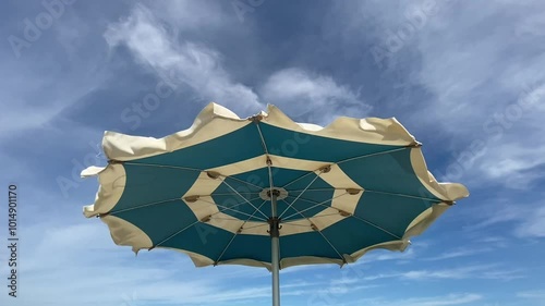 Beach umbrella vawing in the wind in a summer day. blue cloudy sky. low angle image.