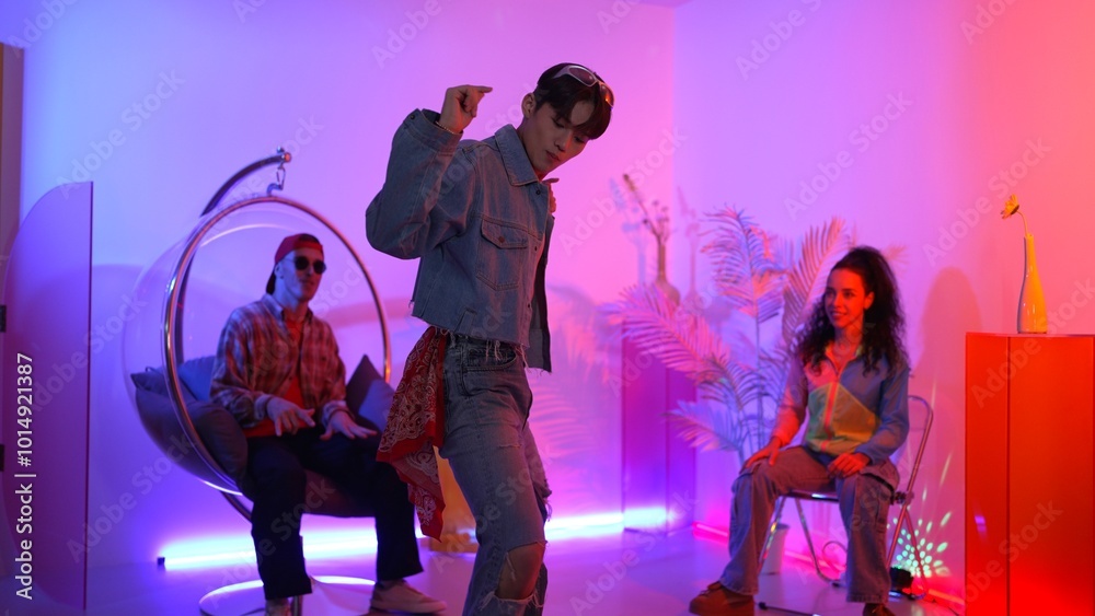 Fototapeta premium Skilled asian dancer moving to modern music while multicultural friend sitting at chair. Professional performer dancing show energetic foot step while hipster team cheering and supporting. Regalement.