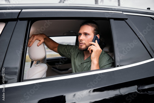 A man talking on the phone from a car window, wearing a green shirt