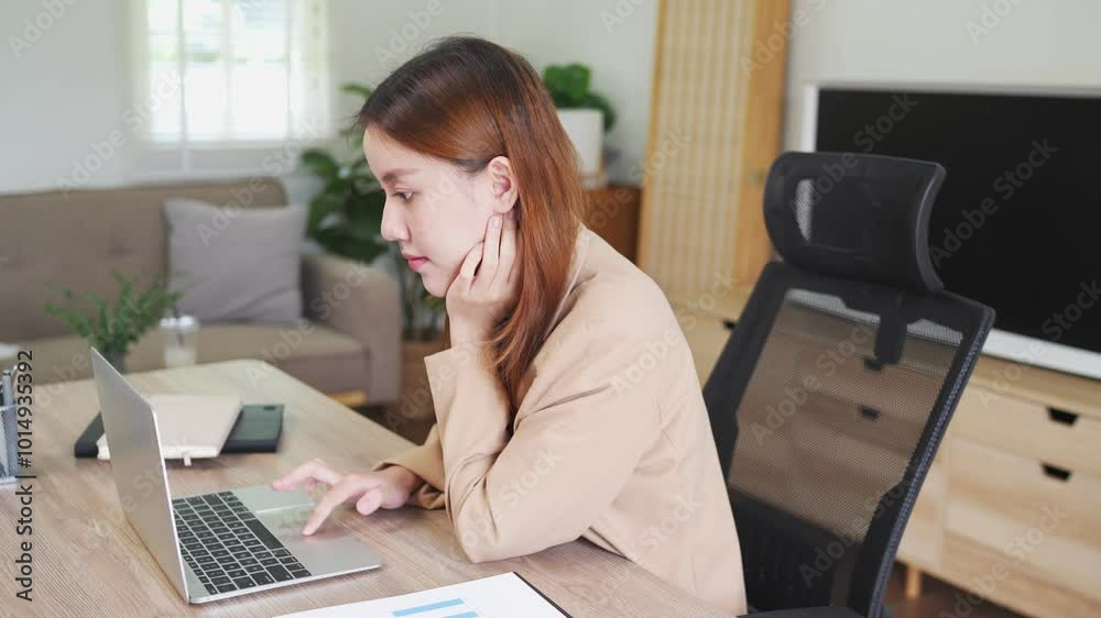 A young woman is sitting at her desk in a modern office, focused on her laptop. She is working in a clean and organized environment, with notebooks and office supplies around her A young woman is sitting at her desk in a modern office, focused on her laptop. She is working in a clean and organized environment, with notebooks and office supplies around her