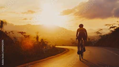 Silhouette of a cyclist riding uphill on a winding road at sunset with beautiful mountain views.