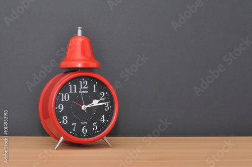Red alarm clock on wood table with black background.