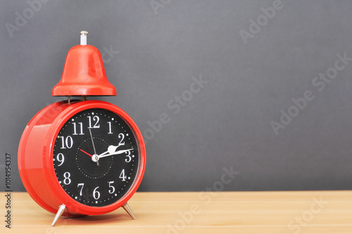 Red alarm clock on wood table with black background.left