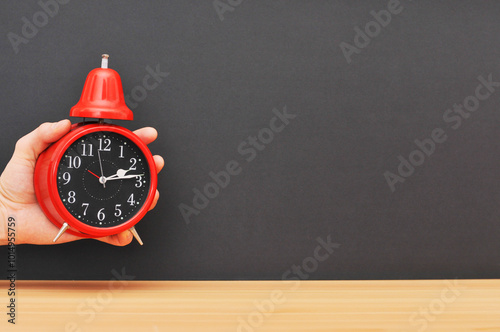 Red alarm clock in hand over wooden table with explosion background.left photo