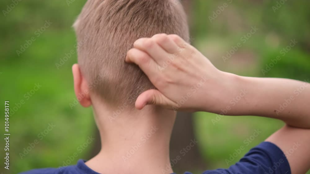 a boy in city park park scratches the back of his head. Closeup caucasian boy a boy in city park park scratches the back of his head. Closeup caucasian boy