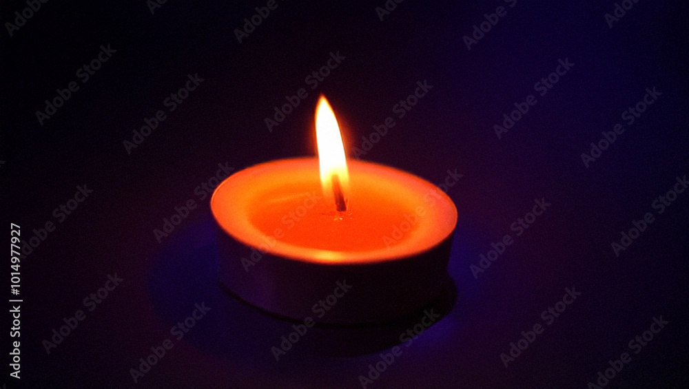 Burning tealight candle in the dark with warm glowing flame Burning tealight candle in the dark with warm glowing flame