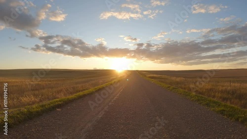 View from the front of a vehicle driving at sunset through open farmland
