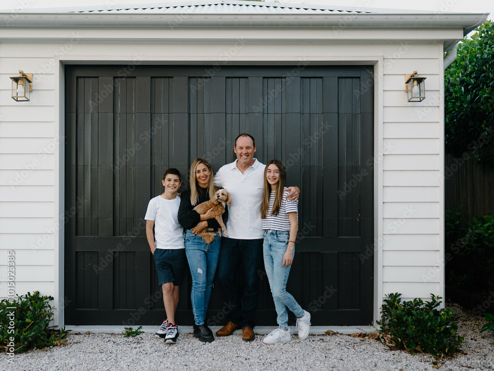Happy family standing outside in front of black garage door with pet dog Happy family standing outside in front of black garage door with pet dog