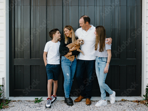 Happy family standing outside in front of black garage door with pet dog photo