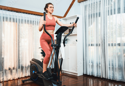 Athletic and sporty woman running on elliptical running machine during home body workout exercise session for fit physique and healthy sport lifestyle at home. Gaiety home exercise workout training.