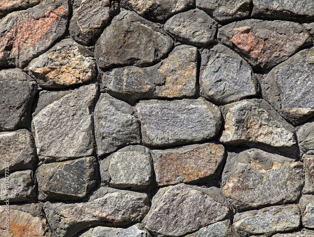 Granite wall, background. Surface of stone structure built of granite rocks (bricks). The wall texture of volcanic grey color. Fence with large gray stones on cement base in the rays of the sun Granite wall, background. Surface of stone structure built of granite rocks (bricks). The wall texture of volcanic grey color. Fence with large gray stones on cement base in the rays of the sun